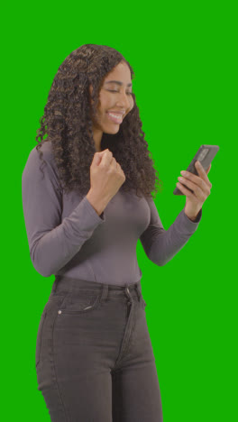 Vertical-Video-Woman-Looking-At-Mobile-Phone-And-Celebrating-Good-News-Against-Green-Screen-4